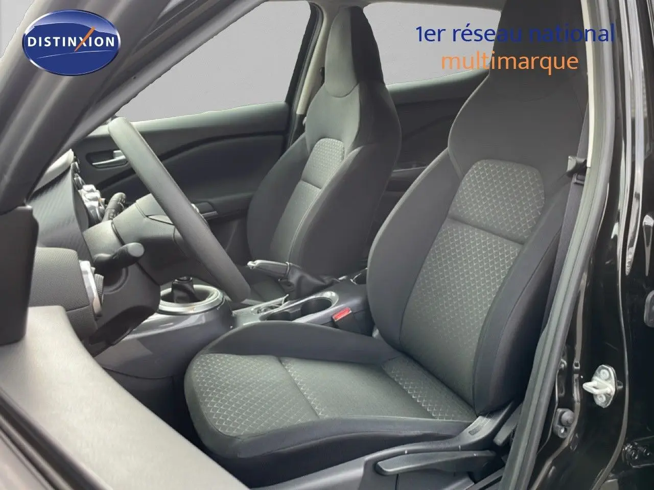 Vue intérieure côté gauche du Nissan Juke noir perle métal 2023, mettant en valeur les sièges en tissu gris noir et la boîte manuelle.