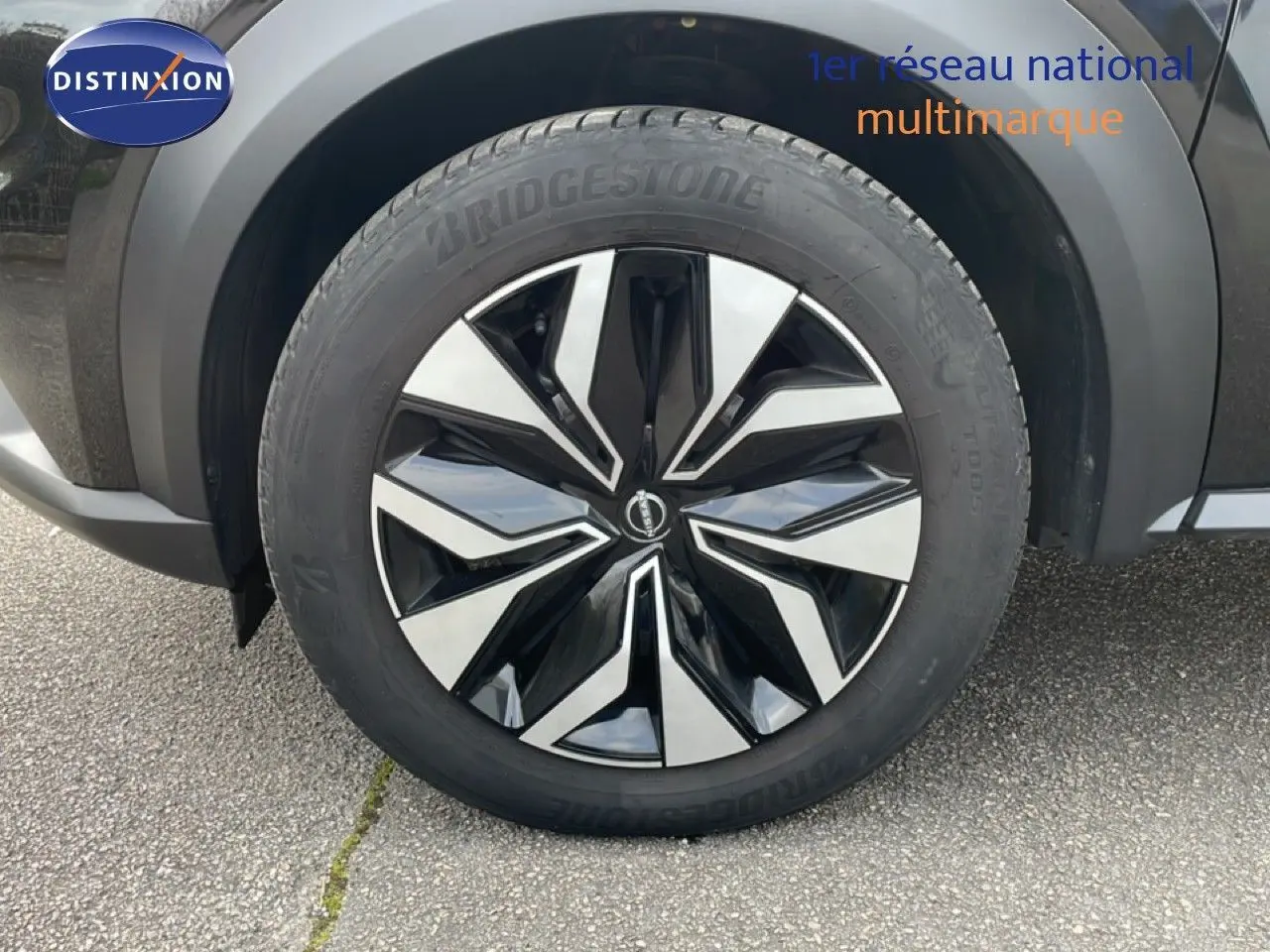 Gros plan sur la roue avant droite d’un Nissan Juke noir perle métal 2023 avec jante noire et argentée.