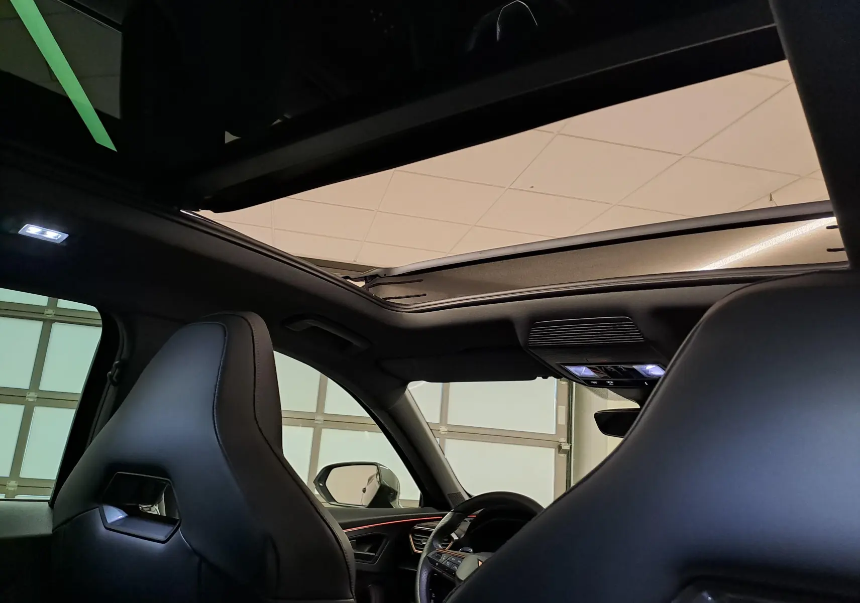 Vue intérieure du toit ouvrant panoramique du CUPRA Formentor noir minuit, avec sièges baquets en cuir et éclairage ambiant.