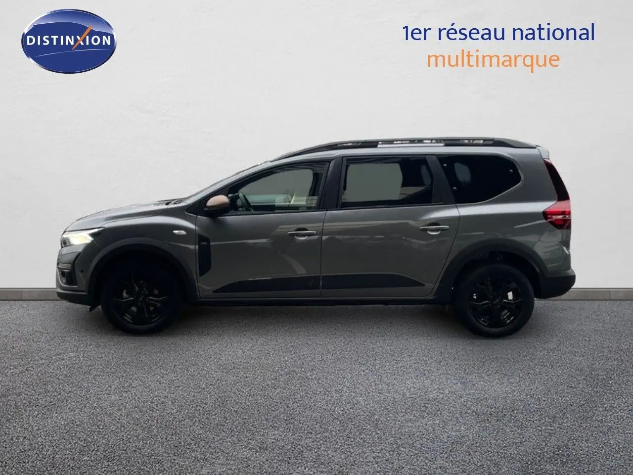 Profil droit du Dacia Jogger gris schiste métal 2026 avec jantes noires et barres de toit visibles.