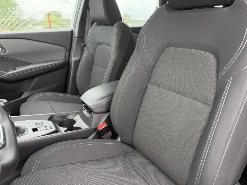 Vue rapprochée des sièges avant noirs en tissu du Nissan Qashqai 2025 avec accoudoir central et console entre les sièges.