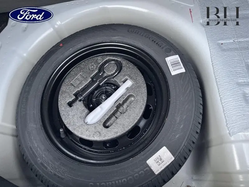 Gros plan sur la roue de secours noire et ses outils dans le coffre d’une Ford Fiesta Blanc Glacier 2022.