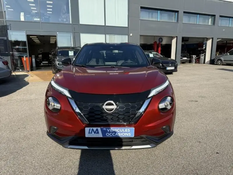 Vue avant d'un Nissan Juke 1.6 Hybrid 2024 rouge Fuji métal avec toit noir, calandre noire et détails chromés.