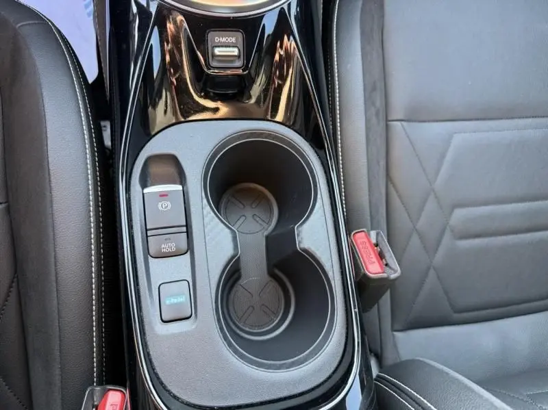 Vue rapprochée de la console centrale noire du Nissan Juke 1.6 Hybrid 2024 avec porte-gobelets et boutons de contrôle.