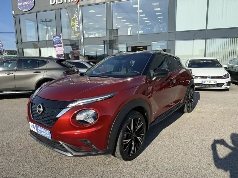 Nissan Juke 1.6 Hybrid 2024 en rouge Fuji métal avec toit noir, vue 3/4 avant mettant en valeur ses jantes noires et son design compact.