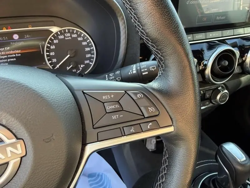 Gros plan sur le volant en cuir noir du Nissan Juke 2024, montrant les commandes de régulateur de vitesse et le tableau de bord partiel.