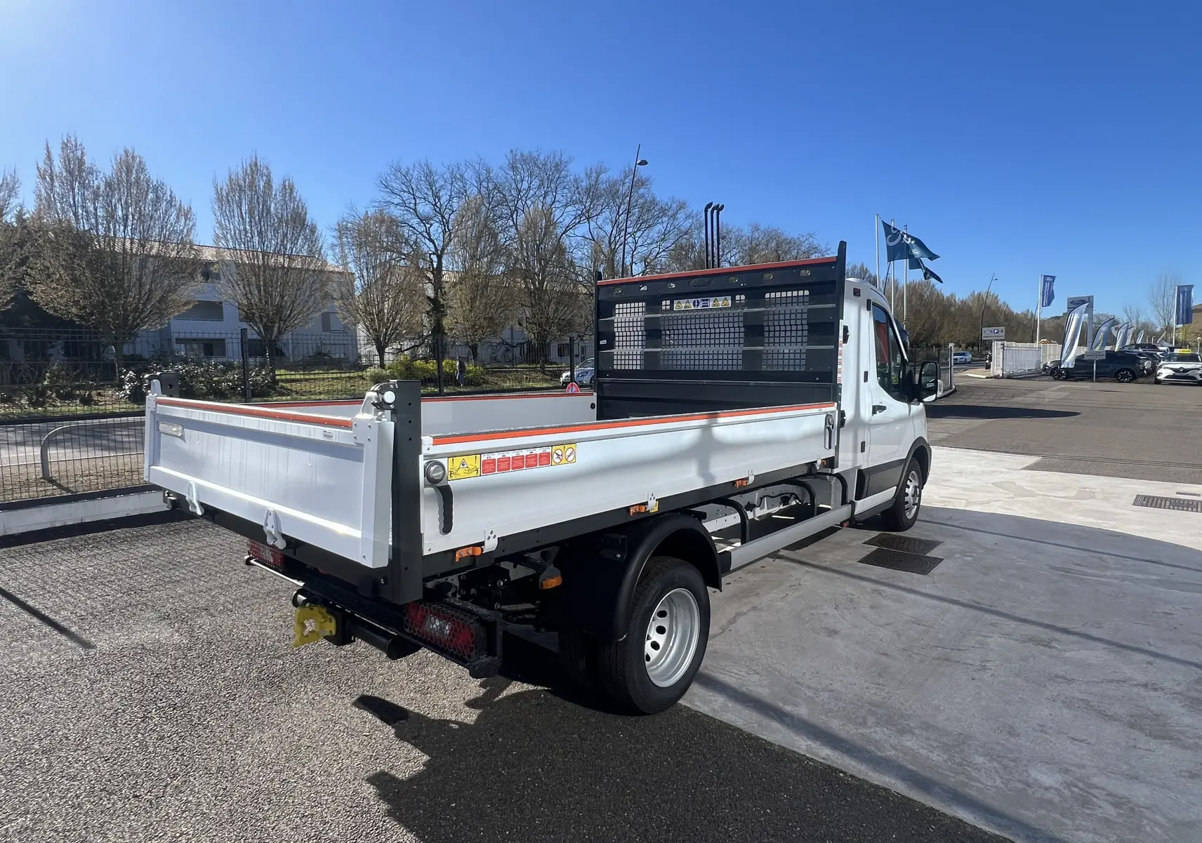 Vue 3/4 arrière droite du Ford Transit Chassis Cabine blanc avec benne et coffre, roues jumelées et grille de protection noire.