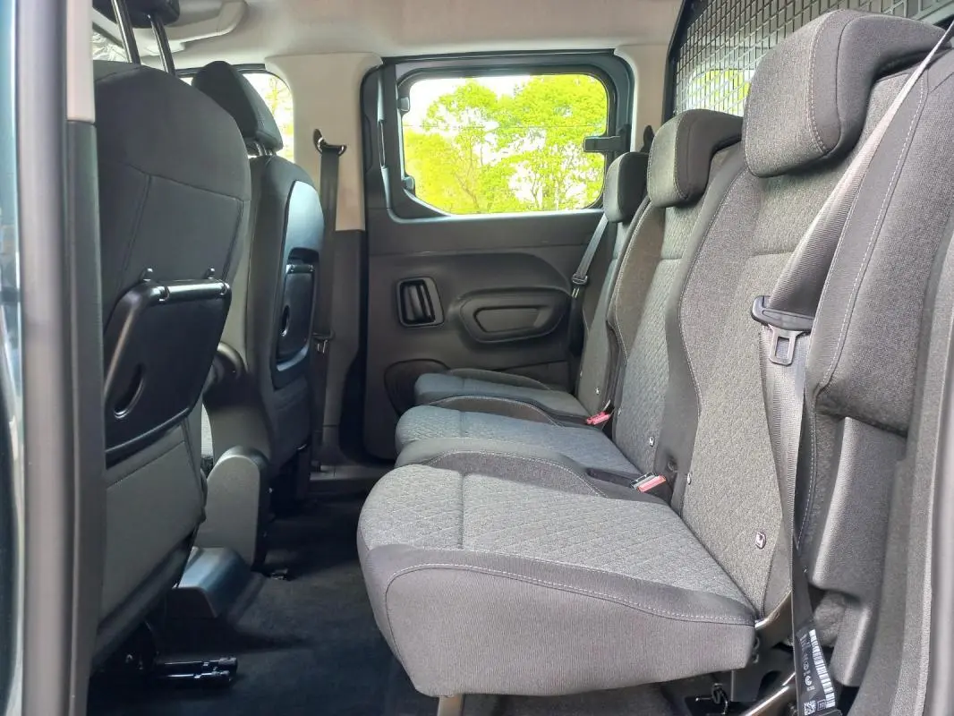 Vue latérale intérieure sur la banquette arrière grise de l’Opel Combo Life M 2025, avec tablettes pliantes au dos des sièges avant.