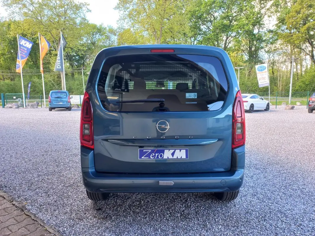 Vue arrière d'un Opel Combo Life M bleu 2025 avec hayon vitré et feux arrière verticaux, stationné sur un sol gravillonné.