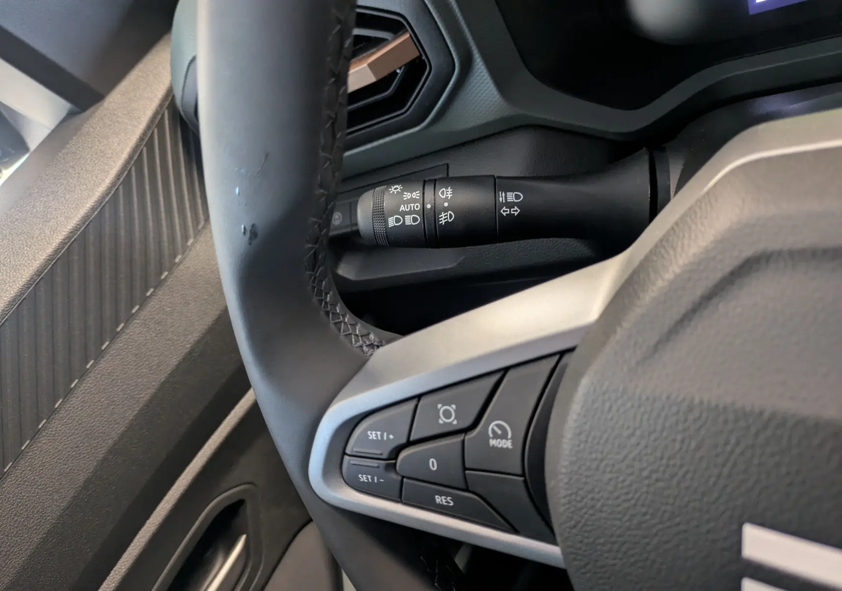 Gros plan sur le volant du Dacia Duster 2025, montrant les commandes de régulateur et le commodo d'éclairage côté gauche.