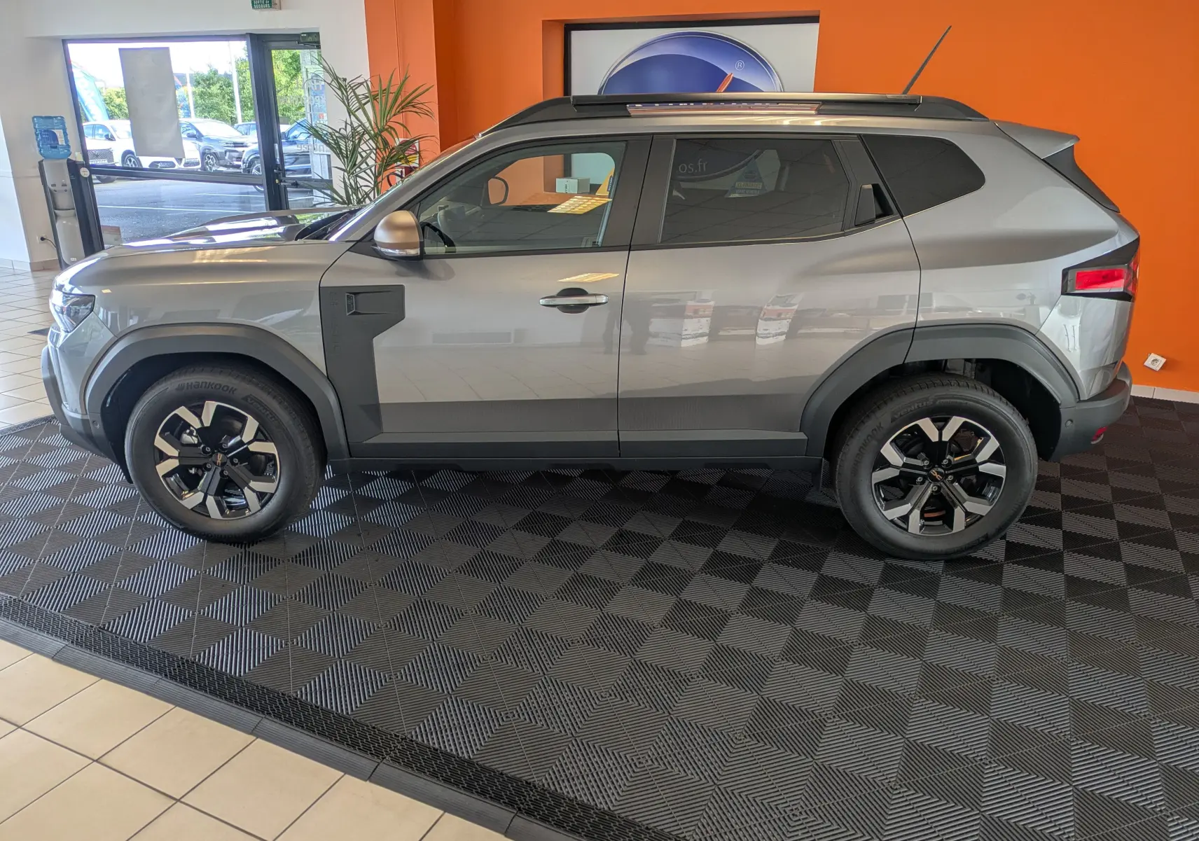 Vue latérale droite d'un Dacia Duster 1.6 Hybrid 140 Extreme gris schiste en showroom avec jantes bi-ton.