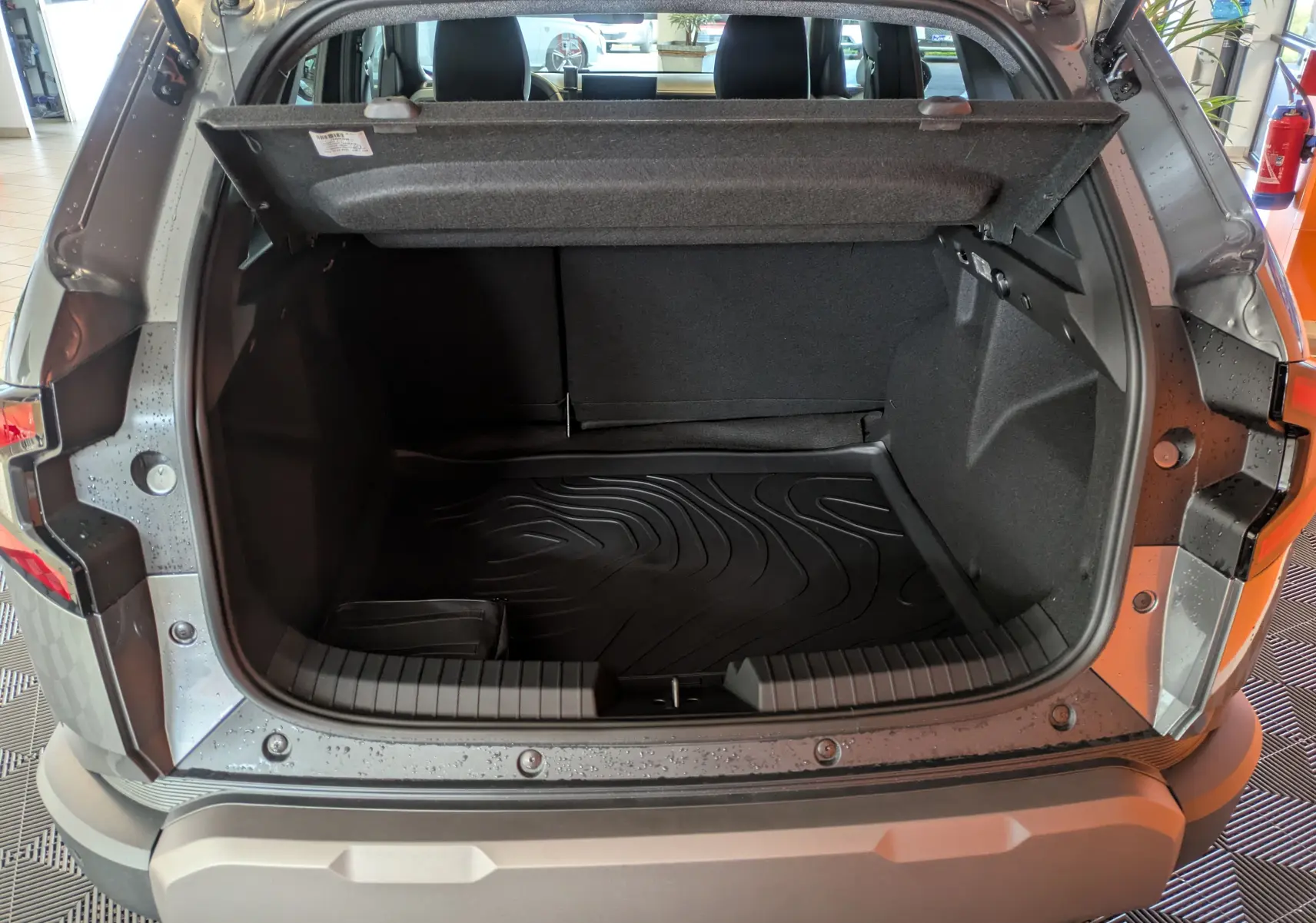 Coffre ouvert du Dacia Duster 1.6 Hybrid 140 Extreme gris schiste, vue arrière montrant l'espace de chargement et le tapis de protection.