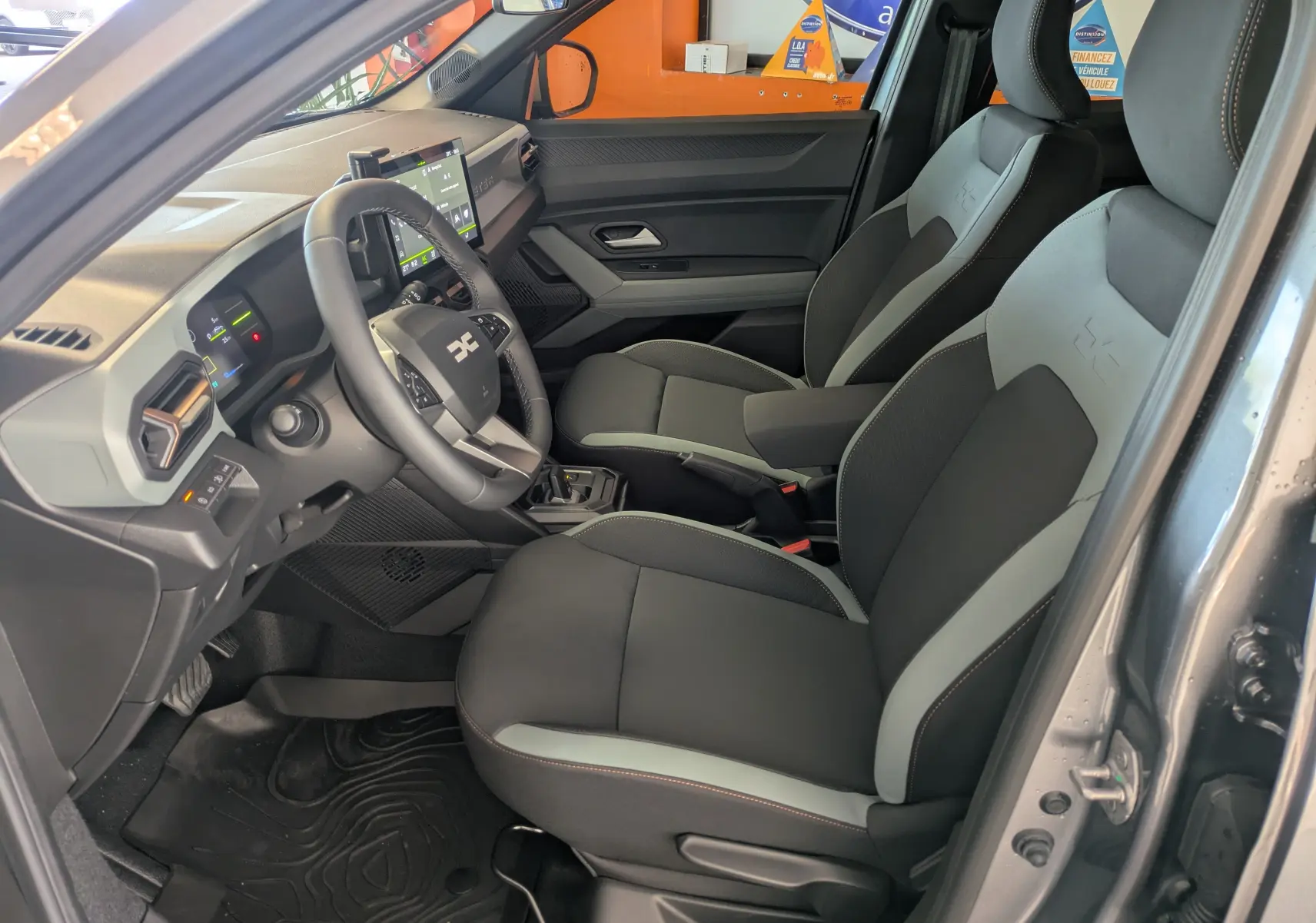 Vue intérieure côté conducteur du Dacia Duster 1.6 Hybrid 140 gris schiste, avec sièges bi-ton et tableau de bord moderne.