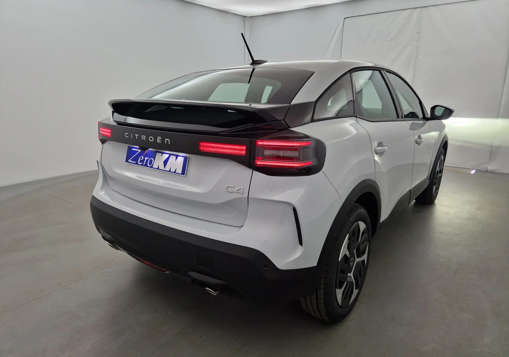 Vue 3/4 arrière droite d'une Citroën C4 2025 blanc okenite avec toit noir et feux arrière LED allumés.