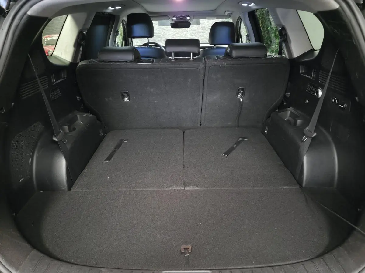 Coffre spacieux du Hyundai Santa Fé 2023 noir avec sièges arrière rabattus et rangements latéraux visibles.