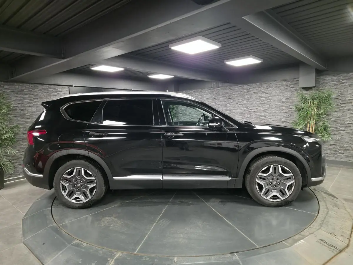 Profil côté gauche du Hyundai Santa Fé 2023 noir métallisé avec jantes alliage et vitres surteintées en intérieur showroom.