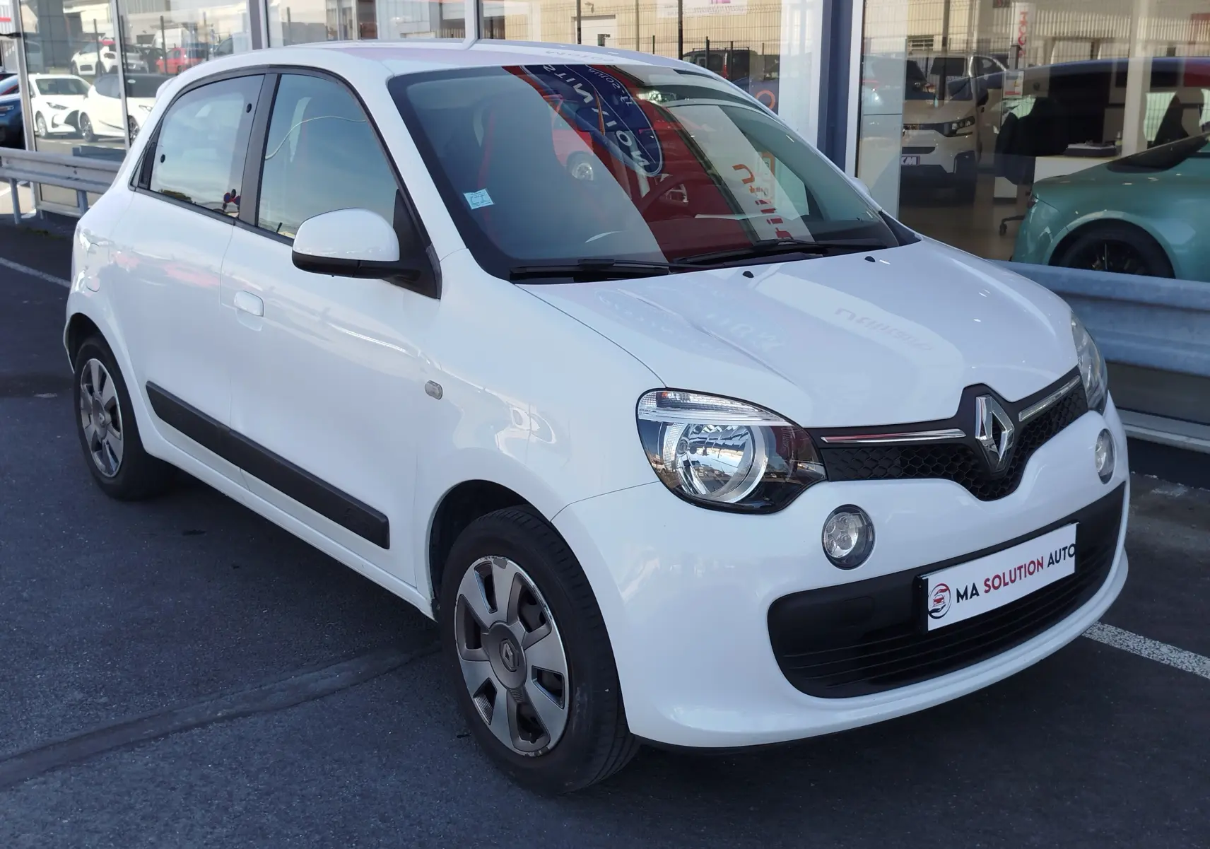 Renault Twingo blanc cristal vue 3/4 avant droit, compacte avec phares ronds et calandre noire distinctive.