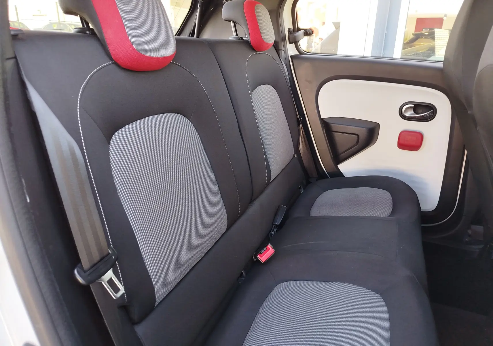 Vue intérieure arrière côté droit de la Renault Twingo blanc cristal, sièges noirs et gris avec appuie-têtes rouges.