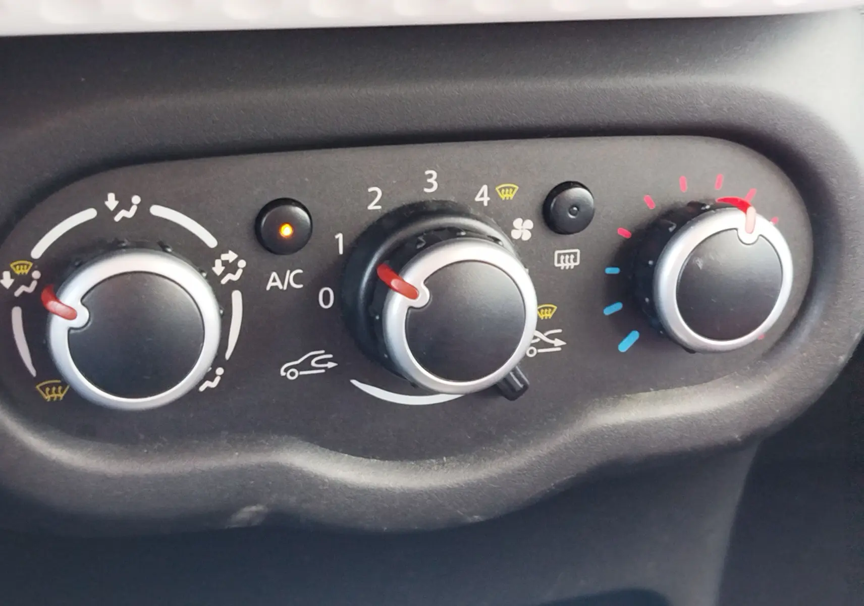 Gros plan sur les commandes de climatisation d'une Renault Twingo blanche, avec réglages de température, ventilation et air conditionné.