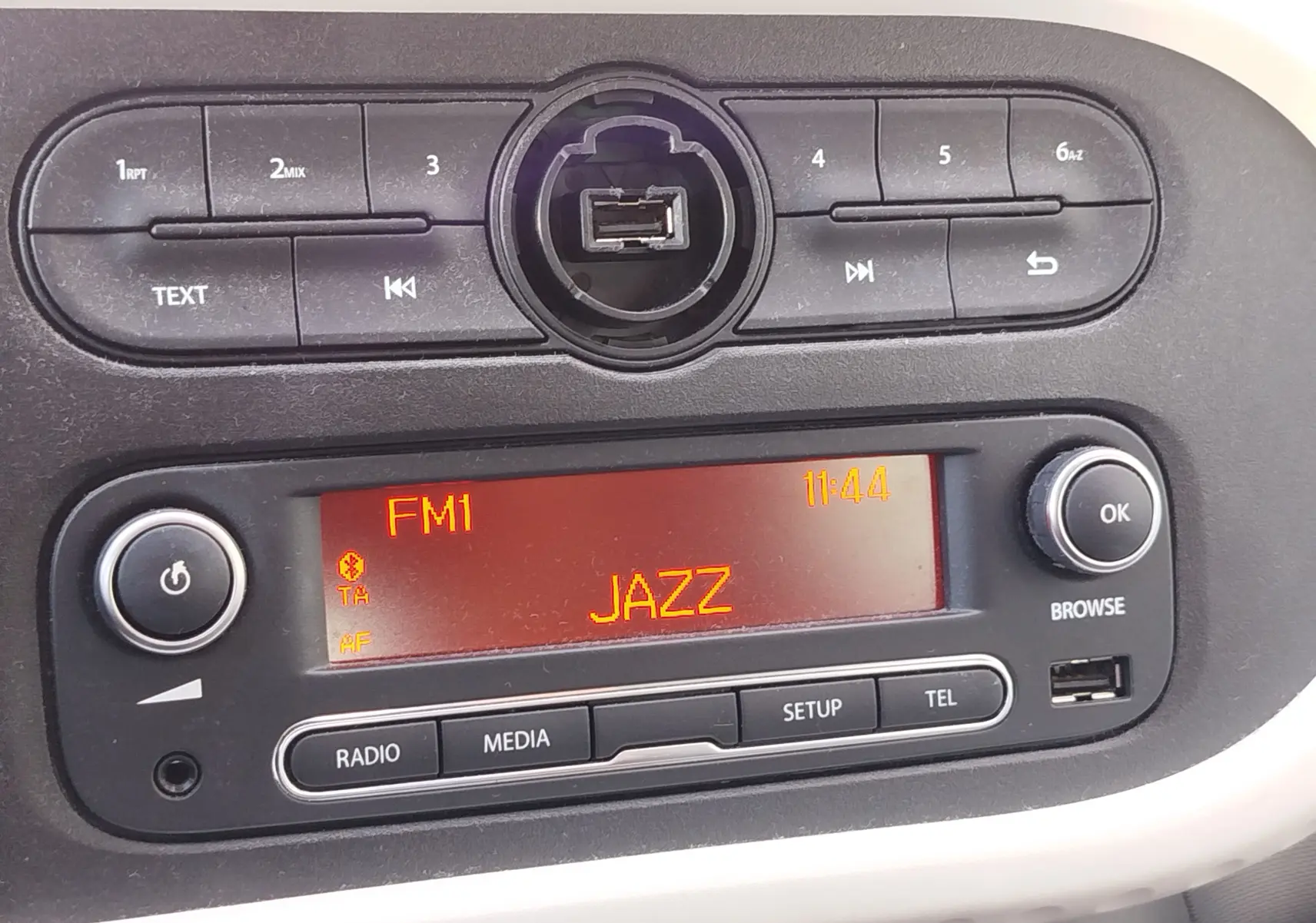 Vue rapprochée de la console centrale noire de la Renault Twingo blanche, affichant la radio FM sur Jazz à 11h44.