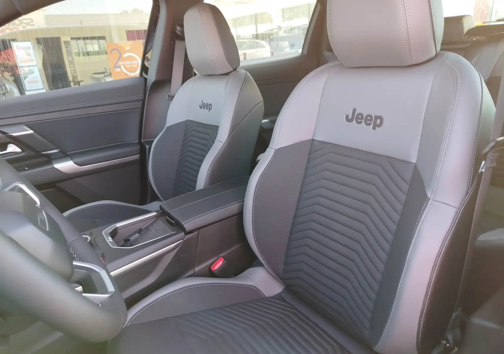 Vue intérieure rapprochée des sièges avant en cuir gris clair et foncé avec logo Jeep brodé sur les appuie-têtes.