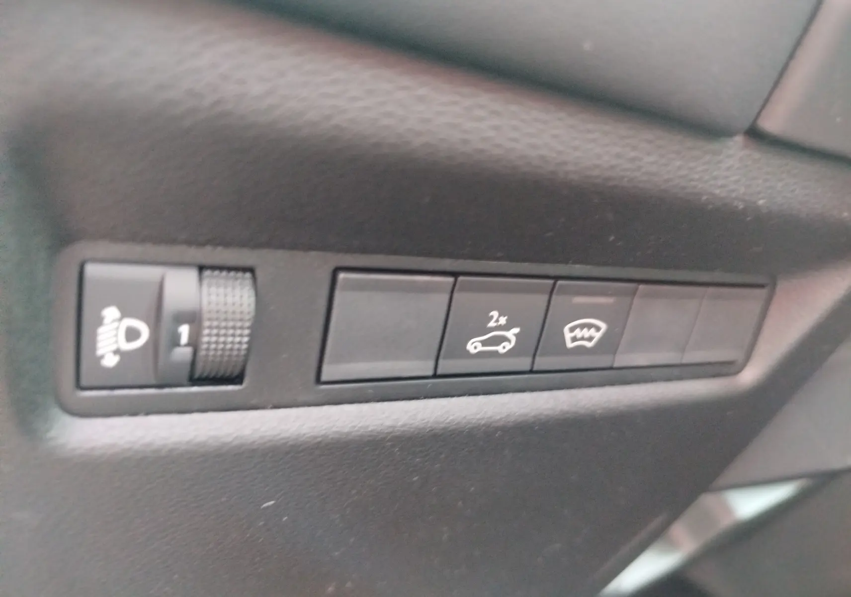 Gros plan sur les boutons de commande intérieurs noirs du Jeep Compass 2026, avec réglage des phares et ouverture du hayon.