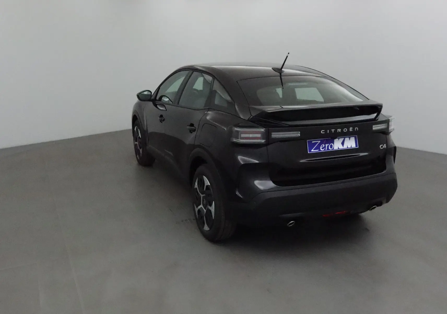 Vue 3/4 arrière gauche d'une Citroën C4 noire 2025 avec feux arrière LED et double sortie d'échappement visible.