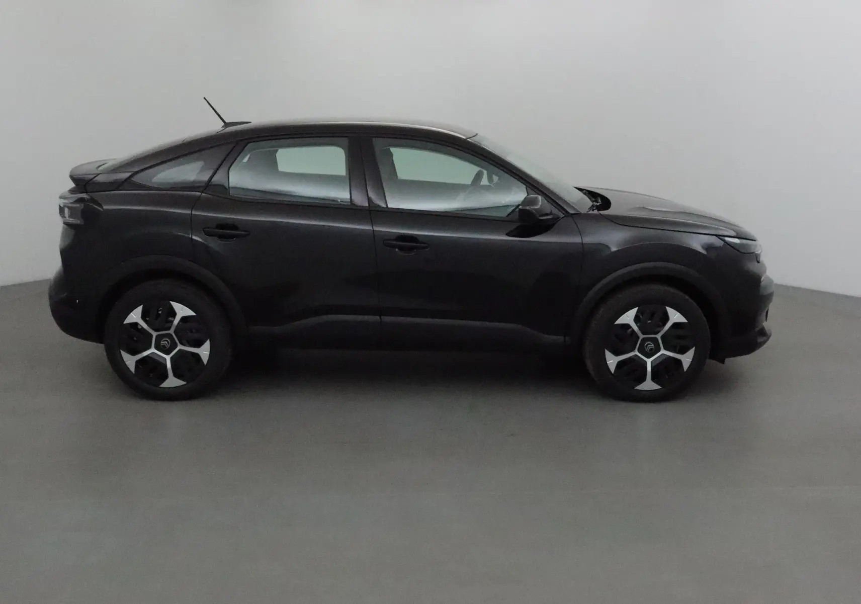 Profil côté gauche d'une Citroën C4 1.2 HYBRID 145 e-DSC6 PLUS noire 2025 aux jantes distinctives en intérieur neutre.