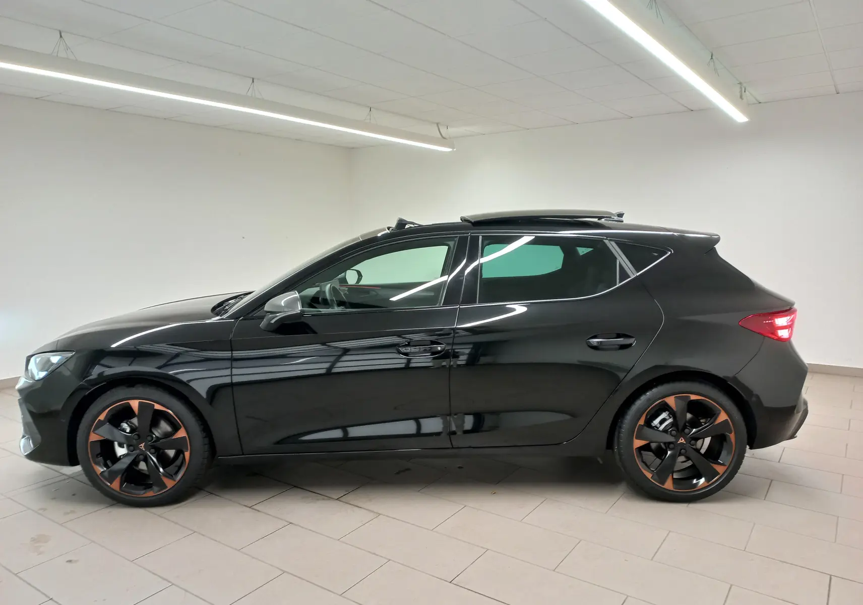 Profil droit d'une CUPRA Leon 2025 noir minuit avec toit ouvrant panoramique et jantes cuivrées 18 pouces en alliage.