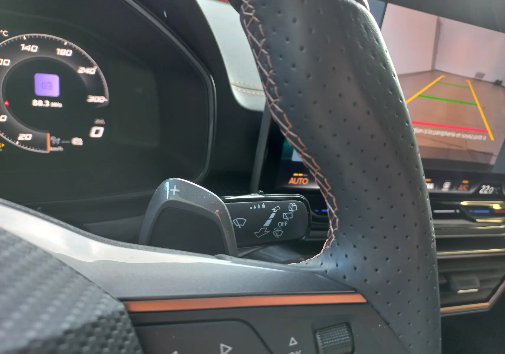 Gros plan sur le volant perforé et les commandes de la CUPRA Leon 2025, avec écran central affichant la caméra de recul.