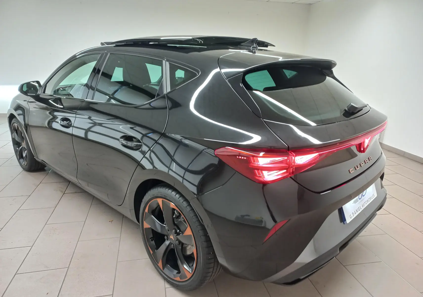 Vue 3/4 arrière droite d'une CUPRA Leon 2025 noir minuit avec toit ouvrant panoramique et jantes cuivrées 18 pouces.
