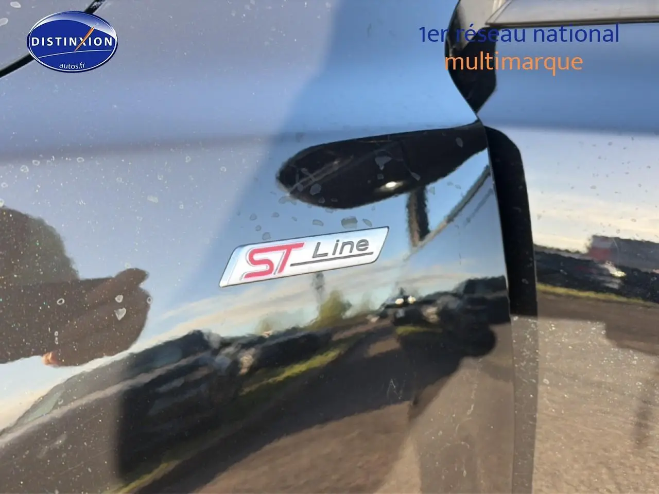 Gros plan sur l'emblème ST-Line sur la porte noire brillante d'une Ford Focus 2024, reflet extérieur visible.