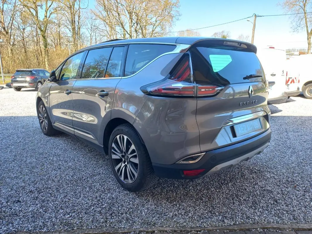 Renault Espace gris vue 3/4 arrière droit, avec feux arrière distinctifs et jantes alliage, stationné sur gravier.