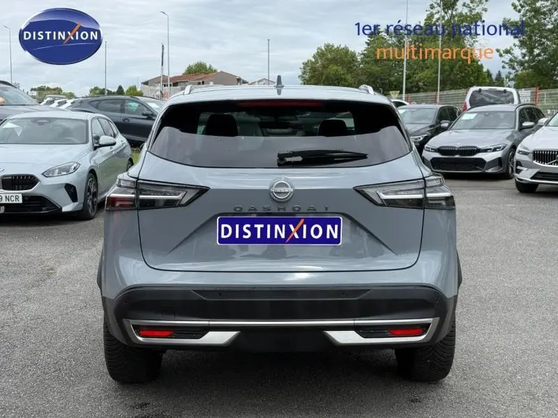 Vue arrière d'un Nissan Qashqai 2025 gris Argile avec feux arrière LED et lunette arrière teintée sur parking.