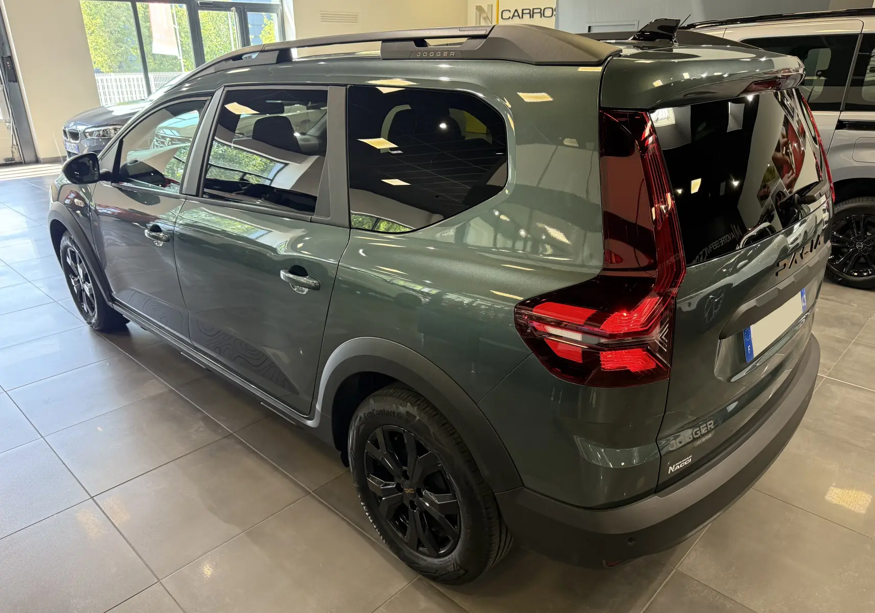 Vue 3/4 arrière droite d'un Dacia Jogger Hybrid 140 Extreme vert cèdre avec jantes noires et barres de toit.
