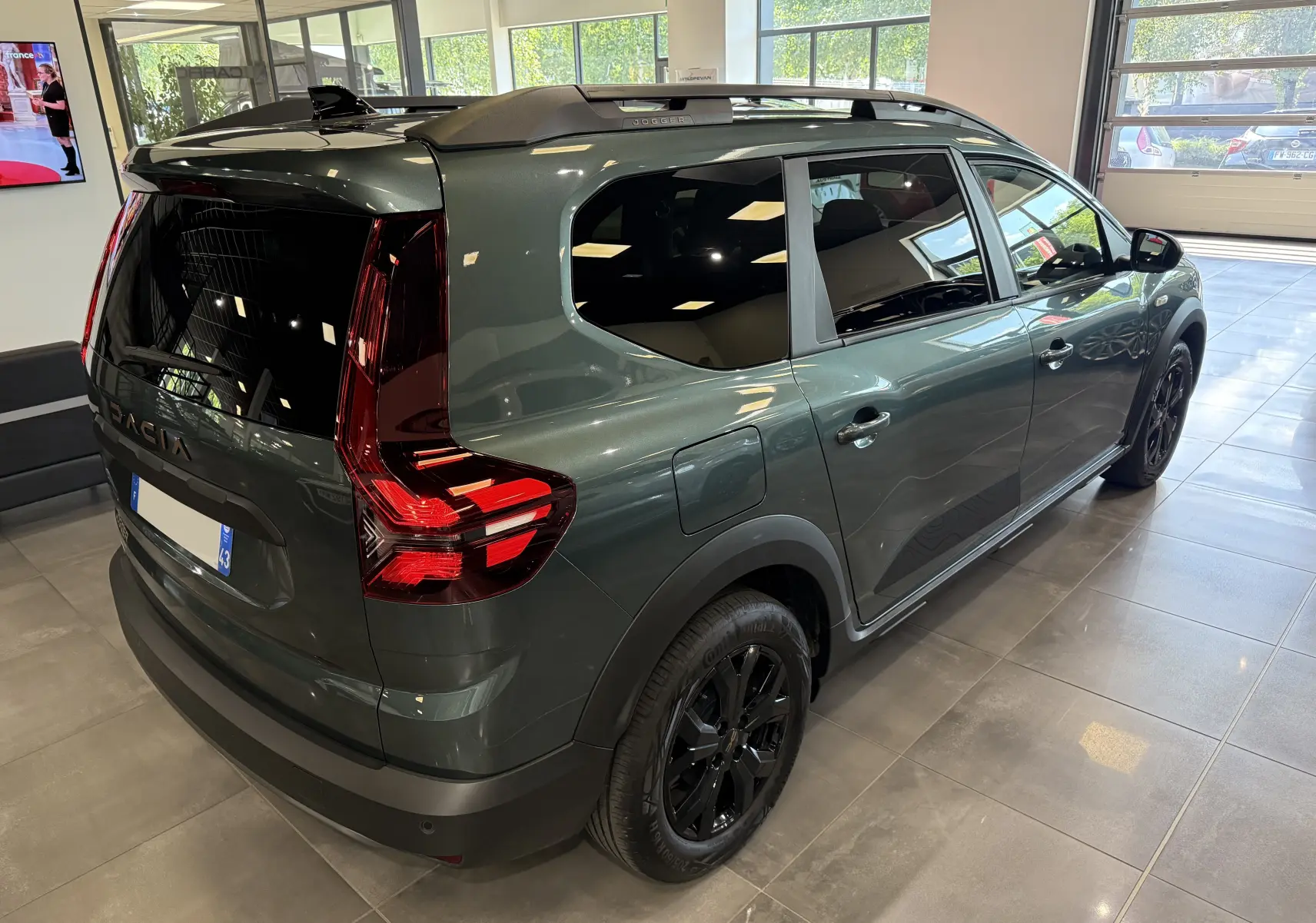 Vue 3/4 arrière droite du Dacia Jogger Hybrid 140 Extreme vert cèdre avec jantes noires et vitres teintées en showroom.
