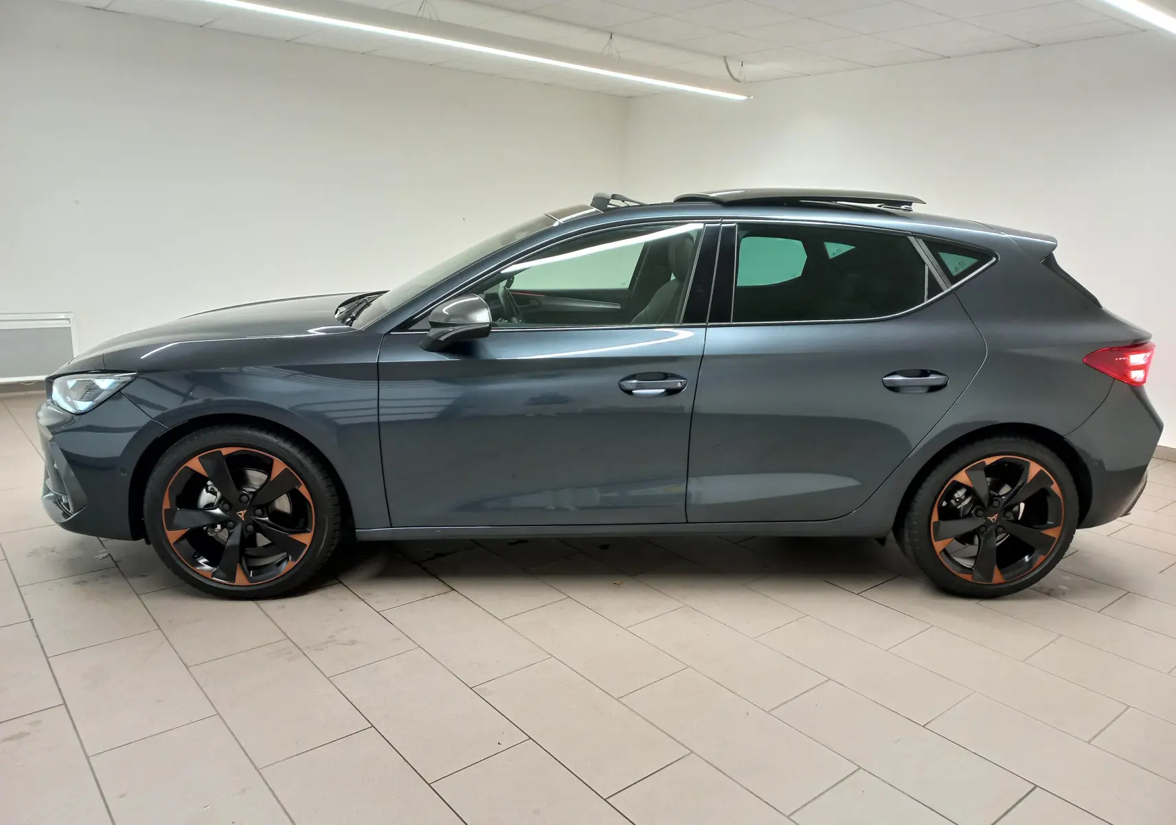 Profil côté gauche d'une CUPRA Leon gris magnétique avec toit ouvrant panoramique et jantes alliage 18'' cuivrées.