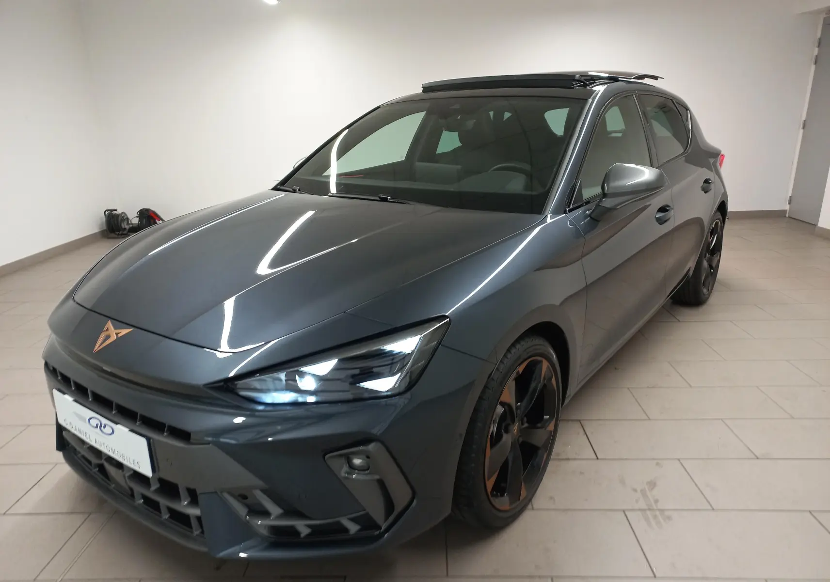 Vue 3/4 avant d'une CUPRA Leon gris magnétique avec toit ouvrant panoramique et jantes alliage noires cuivrées.