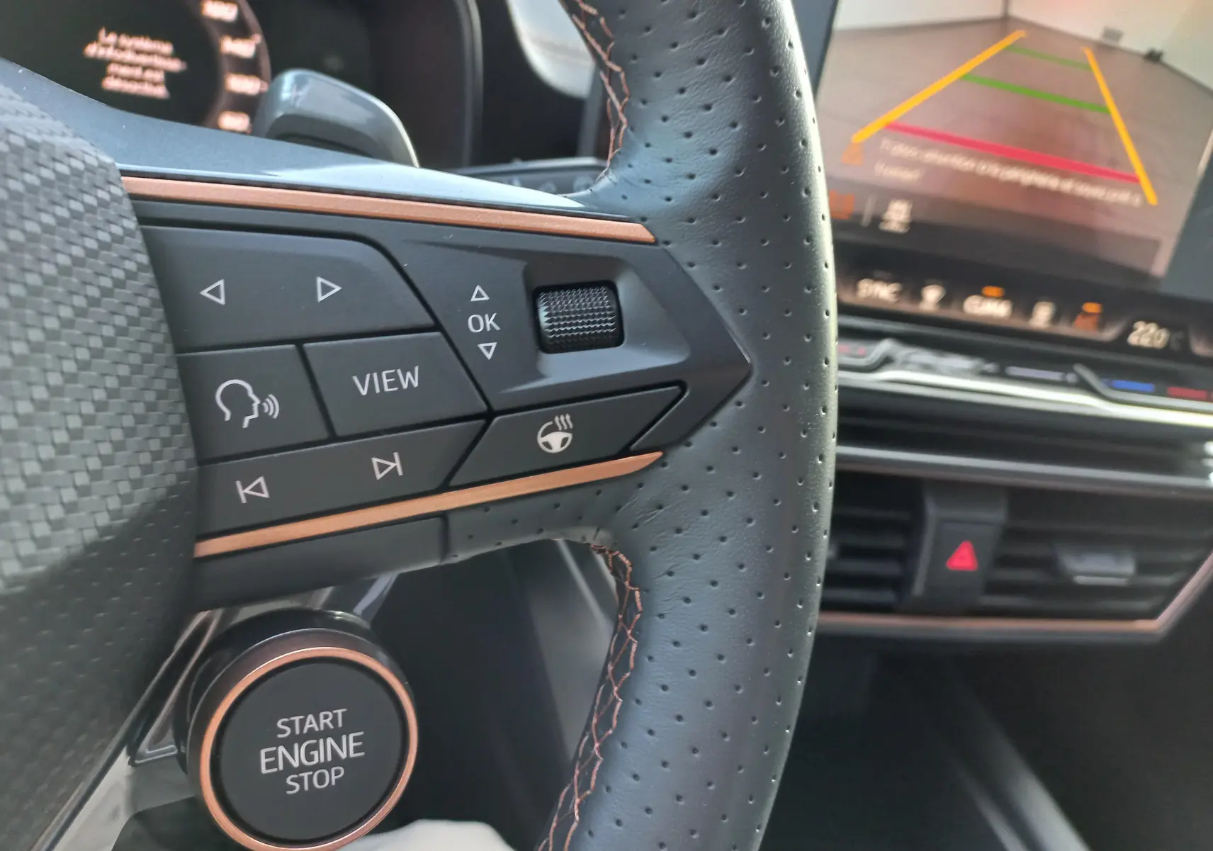 Gros plan sur le volant perforé et les commandes cuivrées d'une CUPRA Leon 2025 avec tableau de bord et écran de recul.