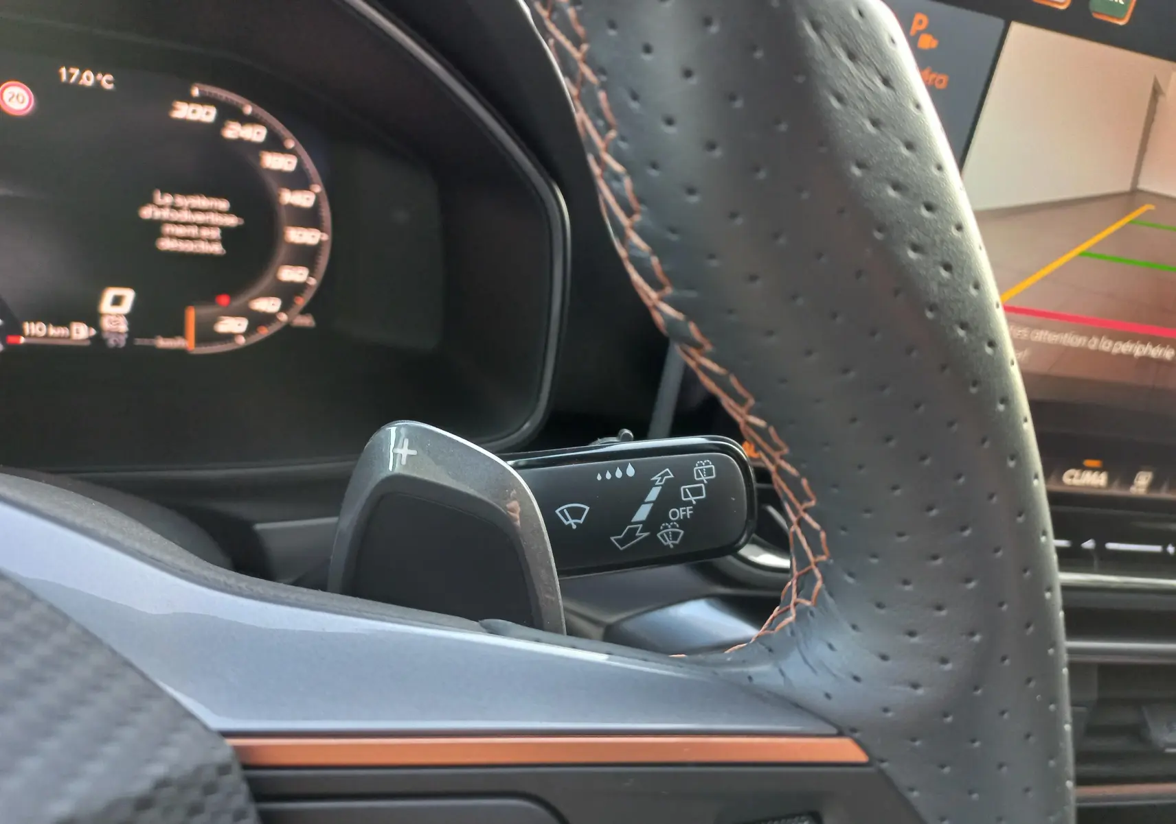 Gros plan sur le volant en cuir perforé avec surpiqûres cuivrées du CUPRA Leon gris magnétique, tableau de bord digital visible.