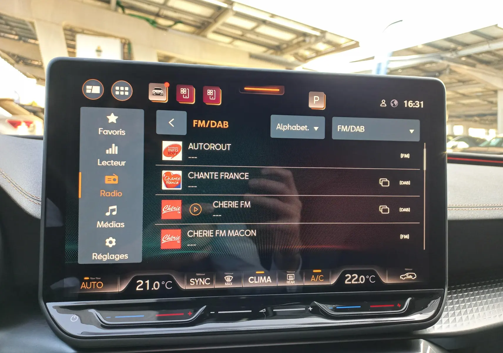 Écran tactile central de la CUPRA Leon 2025 affichant les stations radio FM/DAB avec commandes climatisation en dessous.