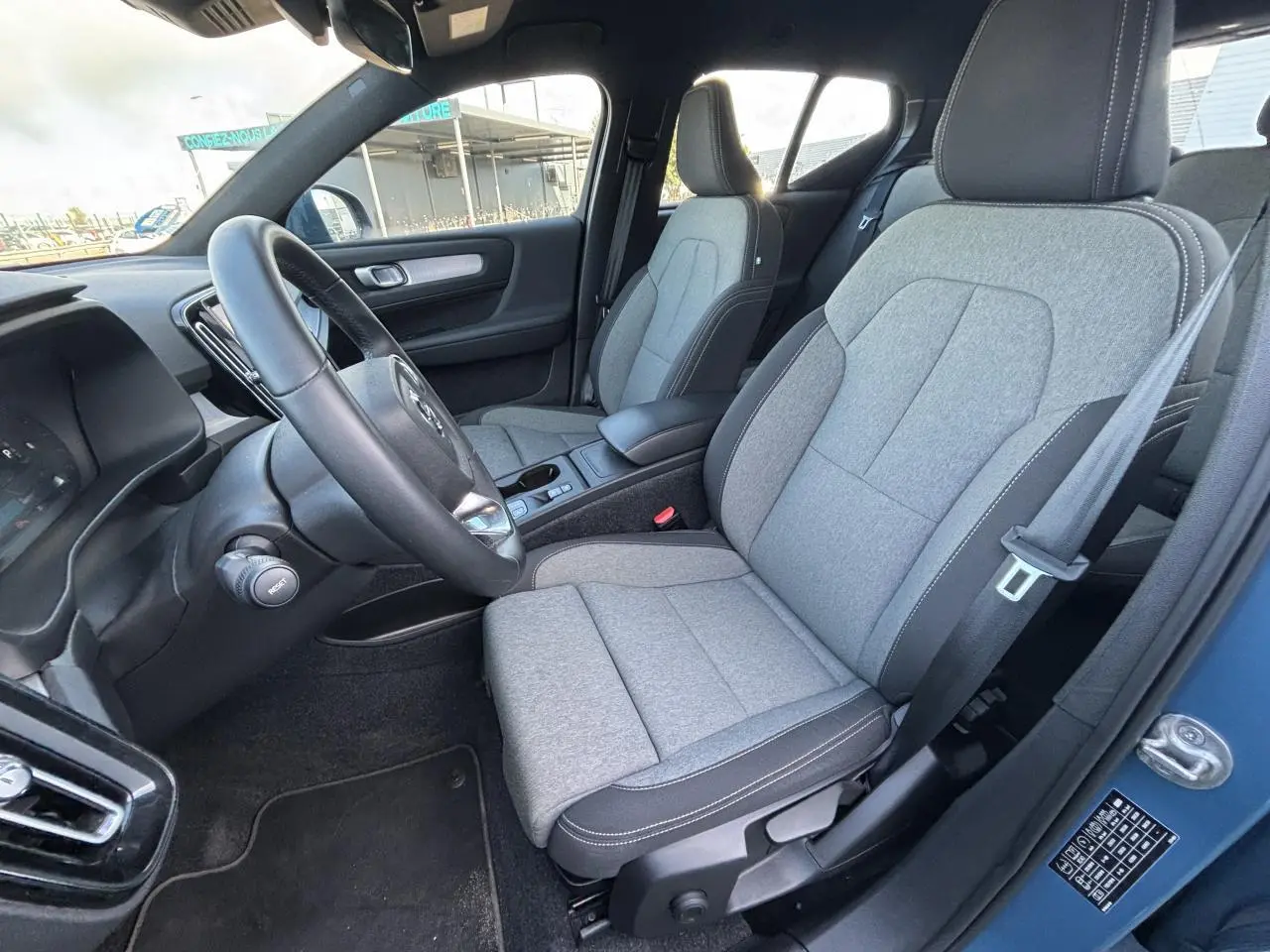 Intérieur avant droit du Volvo XC40 Fjord Blue, sièges tissu gris clair avec volant cuir noir visible.