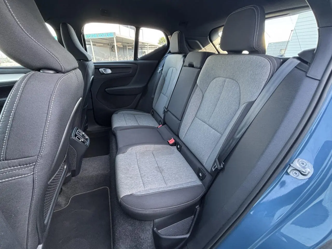 Vue du siège arrière droit du Volvo XC40 Fjord Blue 2024, montrant la sellerie bi-ton grise et noire en tissu et cuir.