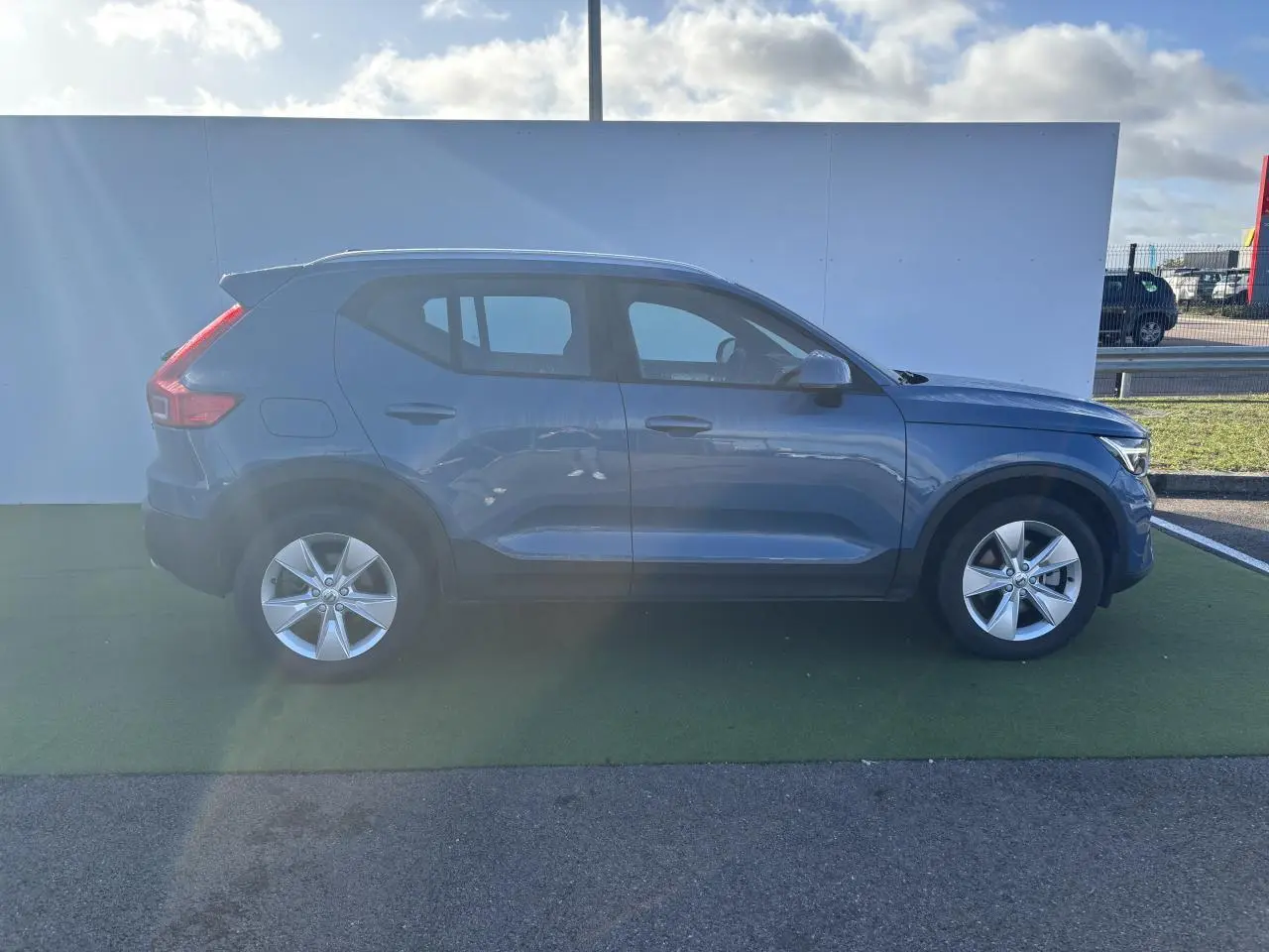 Profil côté droit d'un Volvo XC40 2024 Fjord Blue Metal avec jantes alliage 18 pouces sur fond clair.
