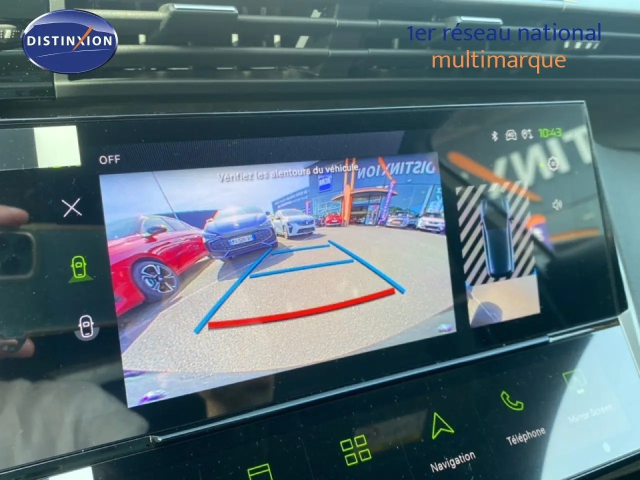 Écran tactile intérieur montrant la caméra de recul avec vue arrière et lignes de guidage bleues et rouges sur un Peugeot 308 blanc.