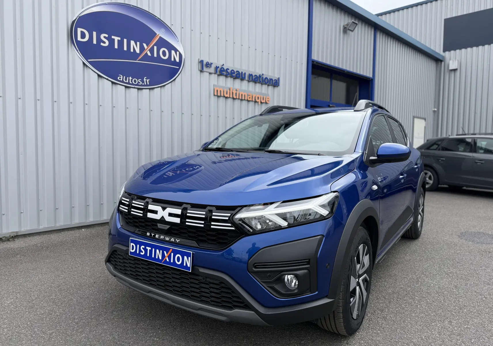 Vue 3/4 avant d'une Dacia Sandero Stepway 2025 bleu Iron avec calandre noire et détails LED distinctifs.