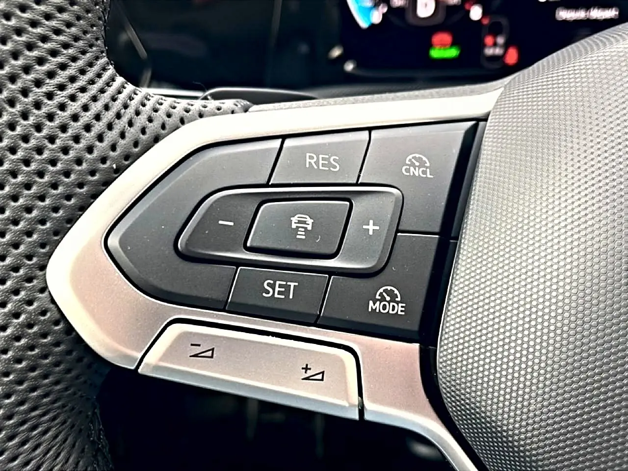 Gros plan sur les commandes multifonctions à gauche du volant perforé de la Volkswagen Golf 1.5 eTSI Evo2 150 R-Line noire.