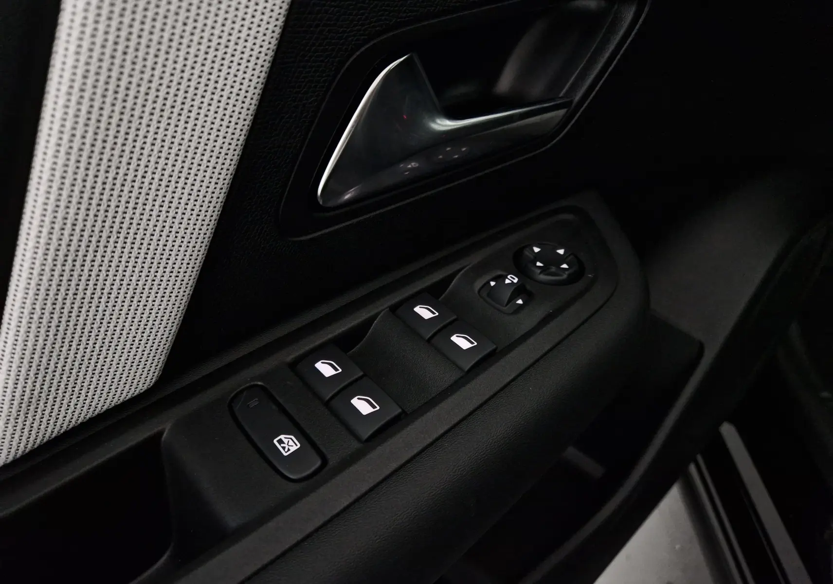 Gros plan sur la commande des vitres et rétroviseurs côté gauche d'une Citroën C4 noire, avec poignée de porte chromée.