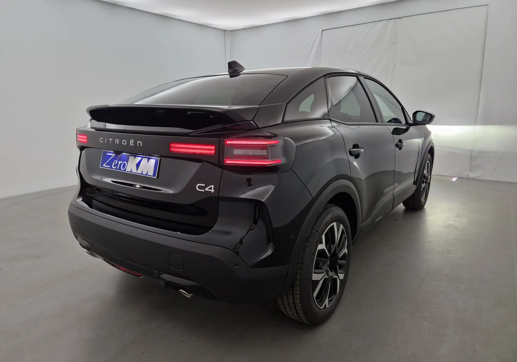 Vue 3/4 arrière droite d'une Citroën C4 noire 2025 avec feux arrière LED allumés dans un studio blanc.