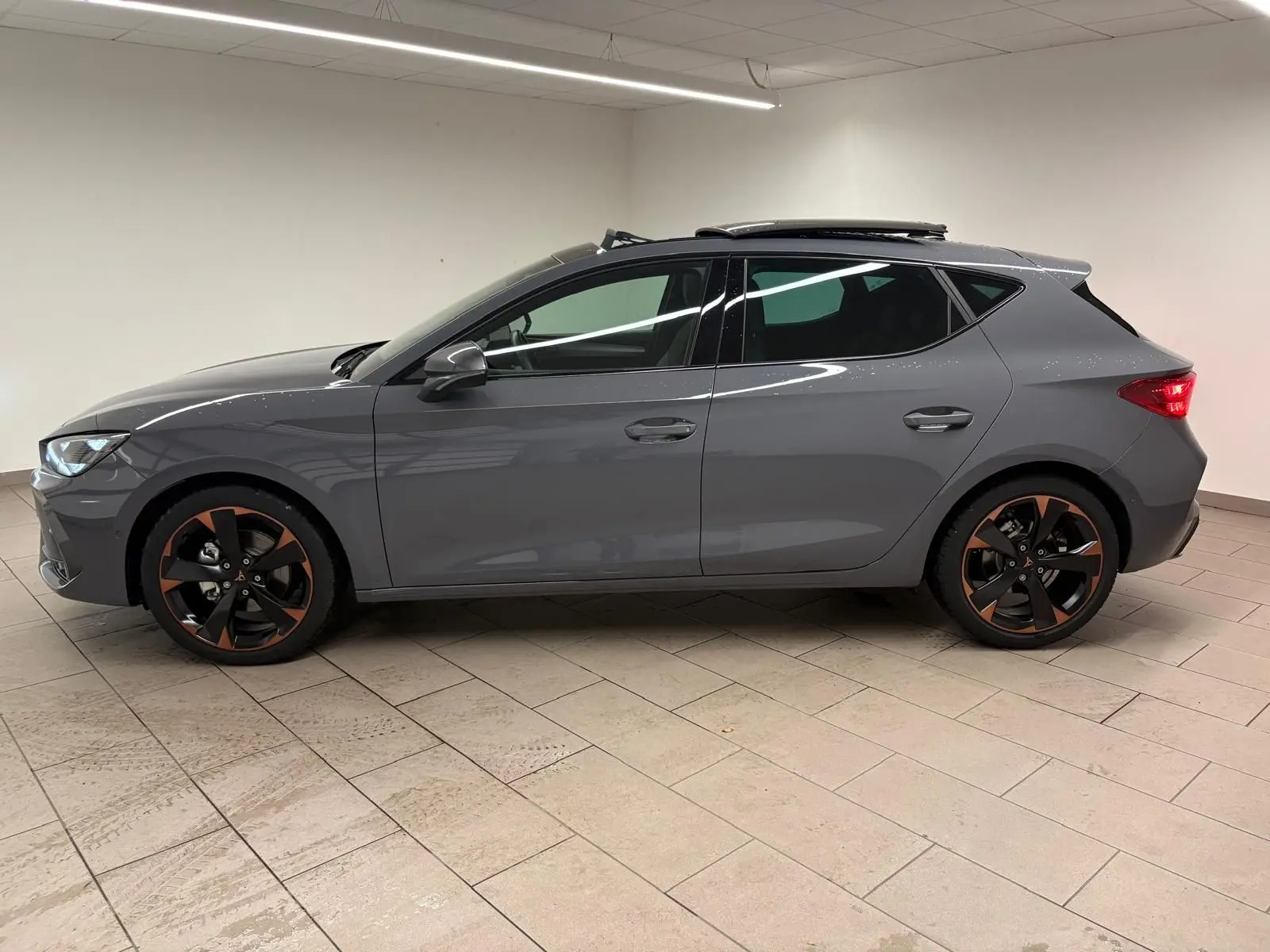 Vue latérale droite d'une CUPRA Leon gris Graphène avec toit ouvrant panoramique et jantes alliage 18'' cuivrées.